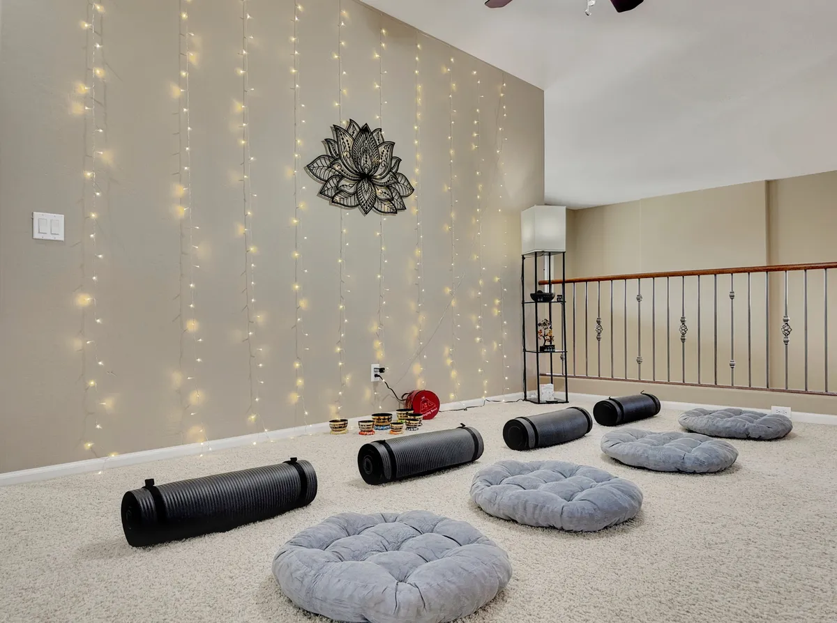 An inviting interior space dedicated to mindfulness, with string lights, lotus wall art, yoga and meditation props, and plush cushions—designed for group yoga classes or meditation sessions.