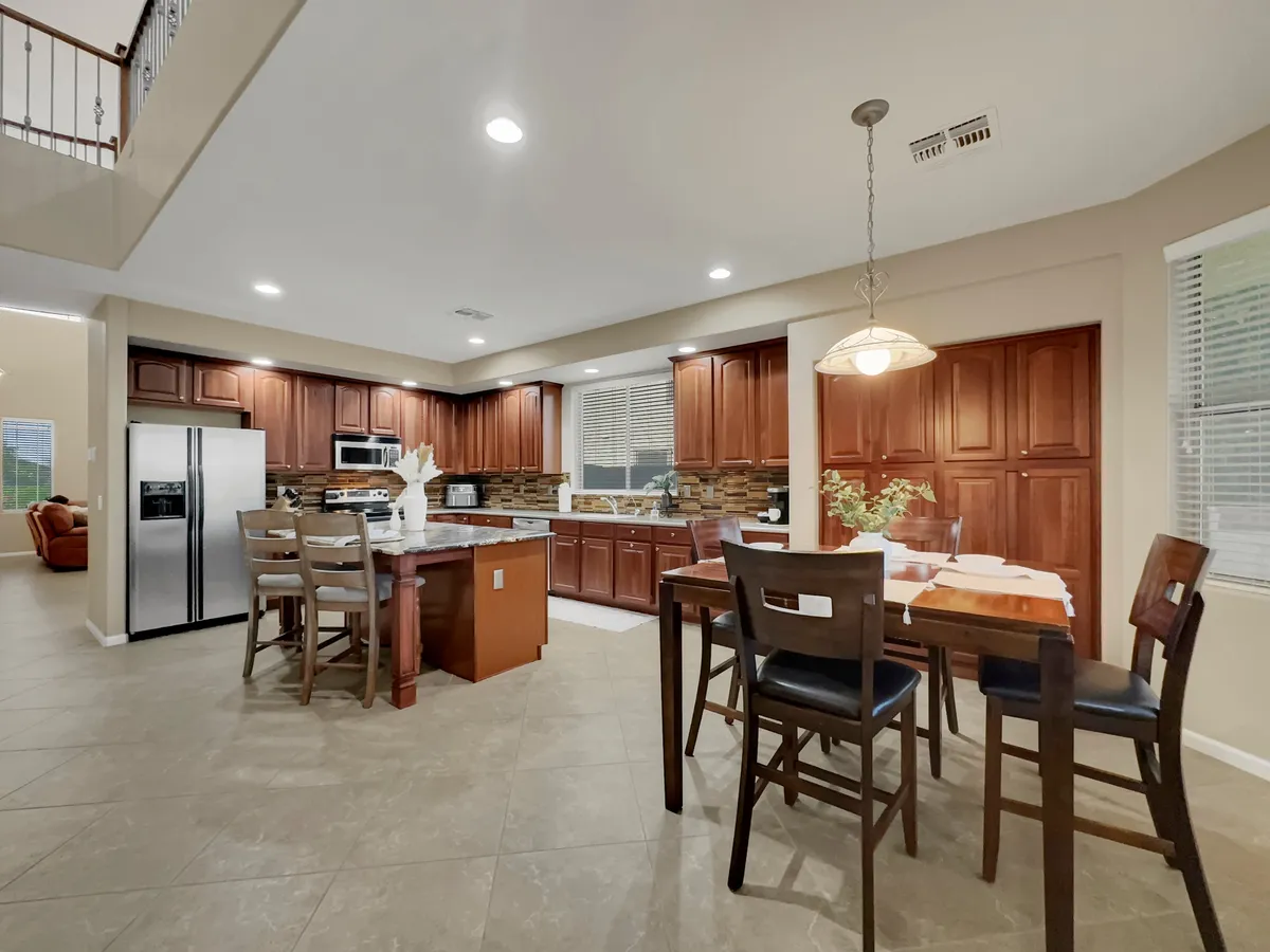 A spacious, modern kitchen featuring a central island, stainless steel appliances, and warm wood cabinetry. The kitchen is open to the adjacent dining area, creating a seamless flow for both cooking and entertaining. Natural light fills the space, enhancing the inviting atmosphere ideal for preparing meals and gathering with family or friends.