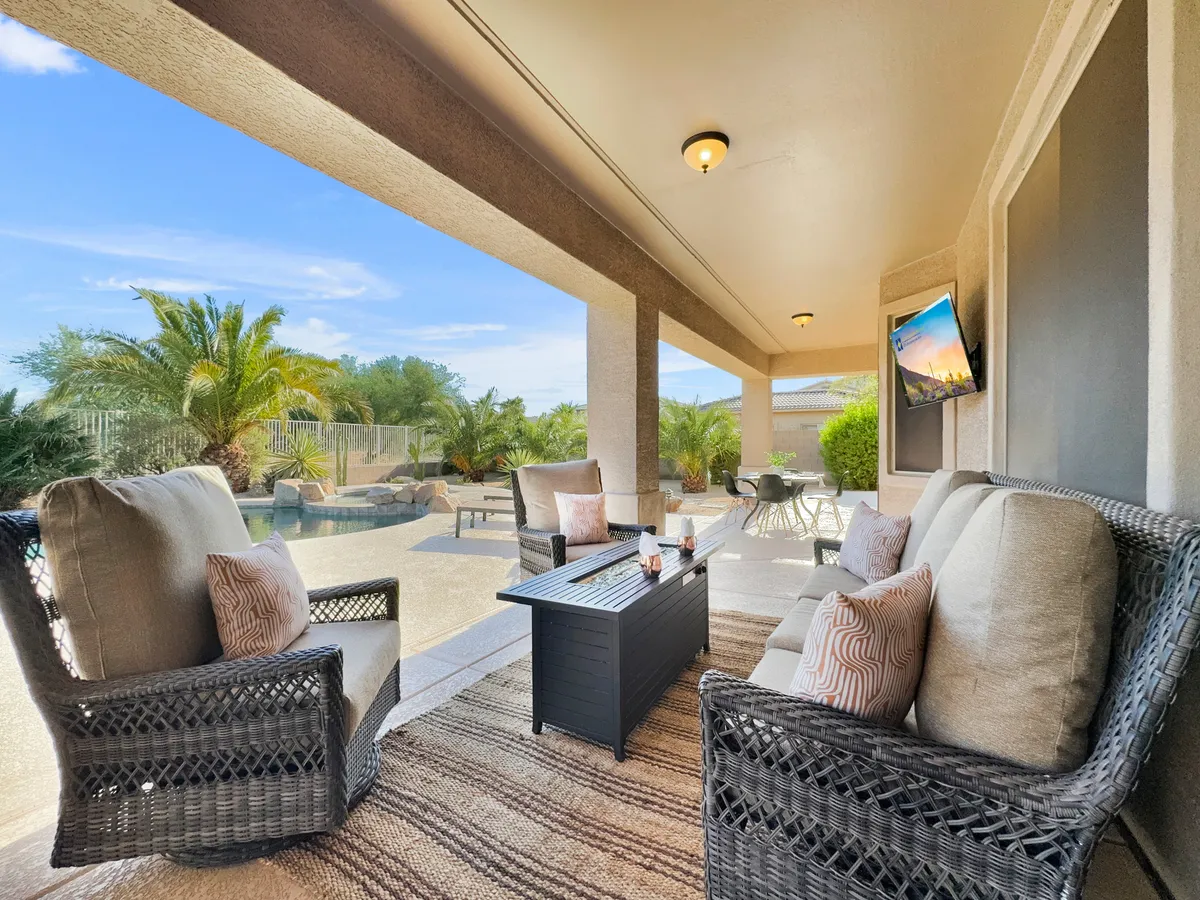 A comfortable outdoor seating area on a patio, with a rug, soft cushions, and a view of the swimming pool and lush tropical plants in the background. The setting is ideal for casual gatherings or quiet afternoons.