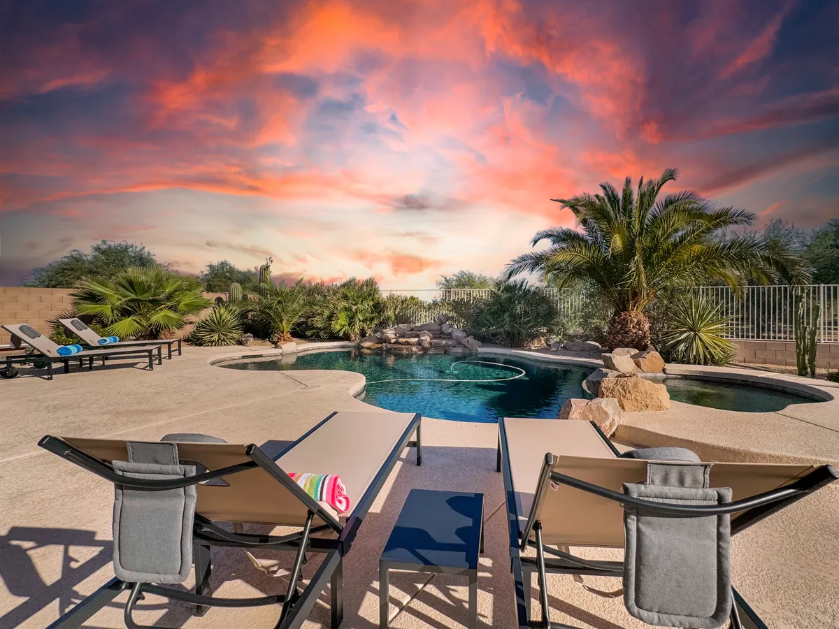 A serene exterior pool scene featuring sun loungers, lush tropical plants, and an inviting blue sky—ideal for relaxation or informal group gatherings after productive sessions. The tranquil setting showcases the property's outdoor amenities for downtime and bonding.