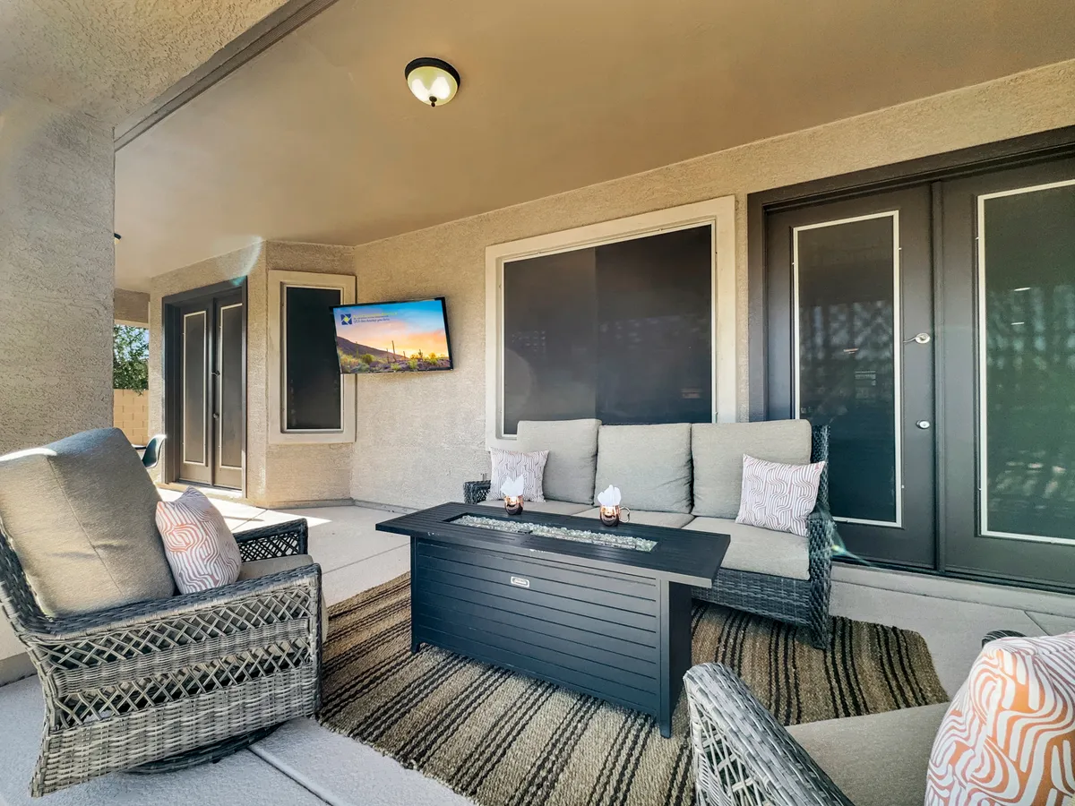 A contemporary outdoor seating area with a cozy arrangement, a coffee table adorned with decorative accents, and a wall-mounted television—suggesting spaces for outdoor meetings, socializing, or casual strategy sessions.