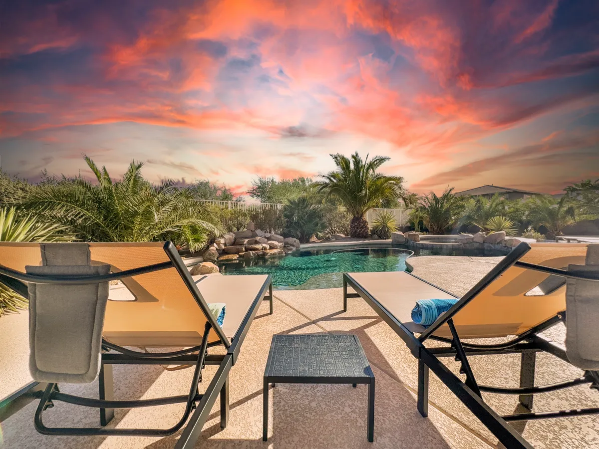 A serene backyard scene featuring a sparkling swimming pool surrounded by lounge chairs and framed by tall palm trees. A vibrant sunset sky sets a warm and inviting tone, perfect for family relaxation or poolside gatherings.