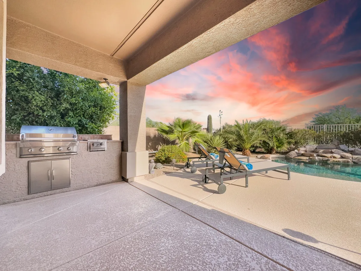 This image features a vibrant exterior scene with a swimming pool as the focal point, flanked by a grill area and comfortable lounge chairs. Lush landscaping frames the pool, creating an inviting spot for both relaxation and active fun. The overall atmosphere suggests a perfect space for barbecuing, swimming, sunbathing, or simply lounging poolside.
