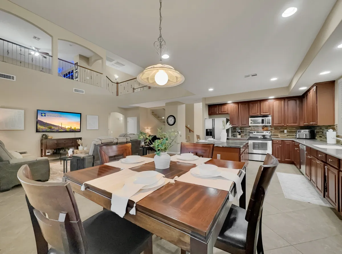 A bright dining area set for a shared meal, with a visible sofa lounge area in the background and kitchen appliances nearby. The arrangement allows for easy movement between dining and living spaces, reinforcing the open-concept design.
