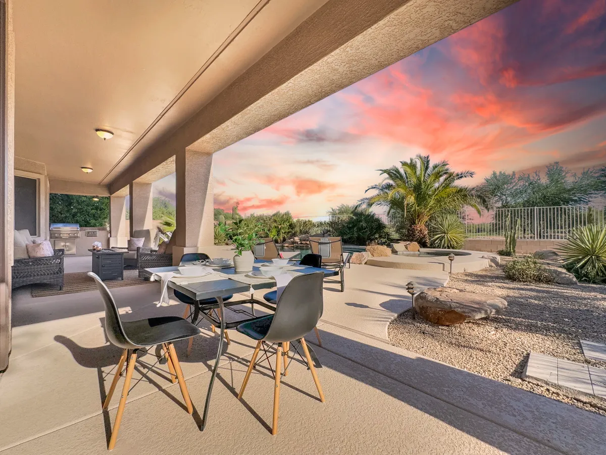 This inviting exterior features a dining table and chairs set amidst a lush, landscaped garden, with a glowing sunset sky overhead. The space is perfect for alfresco dining, relaxing with a book, or hosting intimate outdoor gatherings as dusk falls.