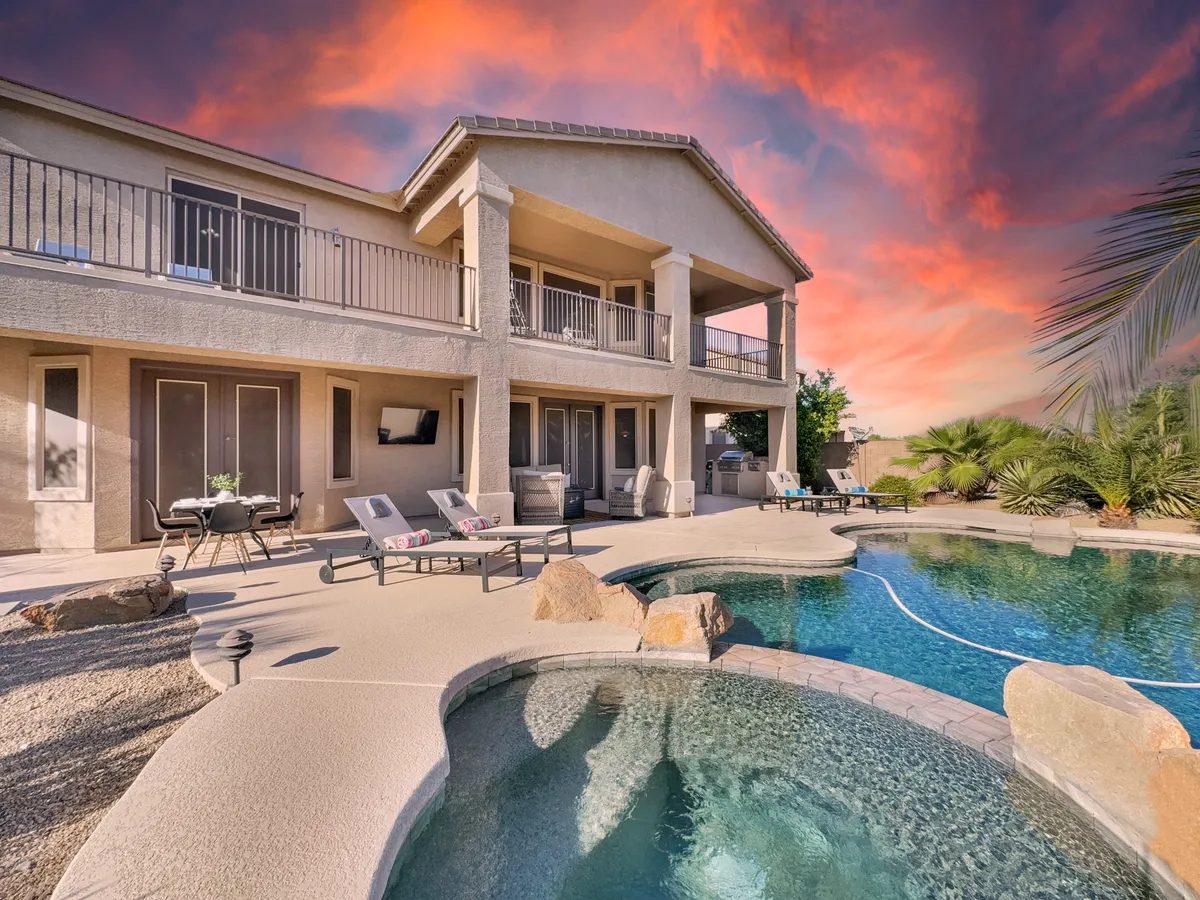 A tranquil outdoor scene featuring a sparkling swimming pool, a comfortable outdoor seating area, a balcony, lush landscaping, and a vibrant sunset sky. The setting exudes relaxation and invites activities such as swimming, sunbathing, and enjoying peaceful evenings outdoors.