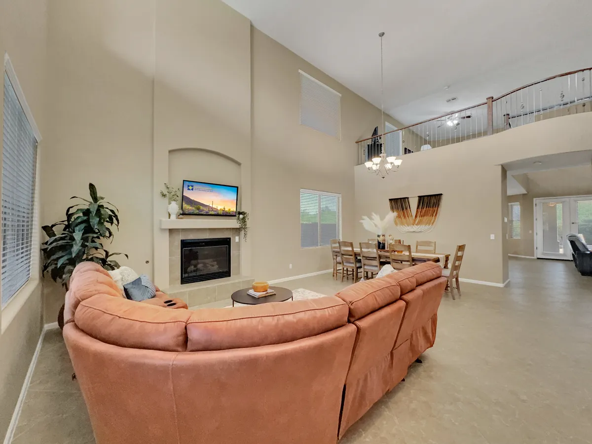 A spacious, open-concept living area featuring a large sectional sofa, a glowing fireplace, a wall-mounted TV, a dining area with a table and chairs, and expansive windows framing a lush golf course view. Warm, inviting lighting and stylish décor create a welcoming atmosphere.